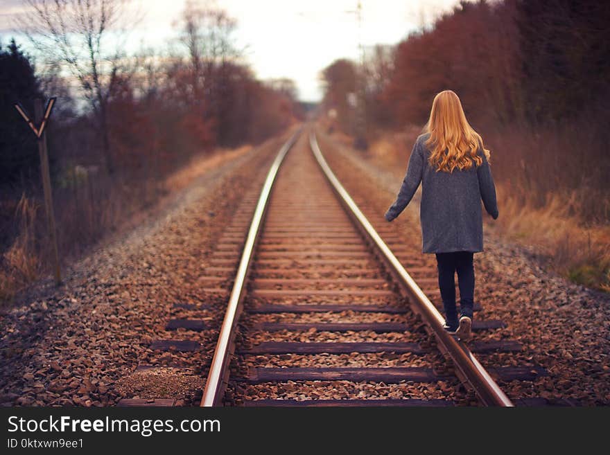 Woman in Blue Jacket and Blue Jeans Walking on Train Track Photography