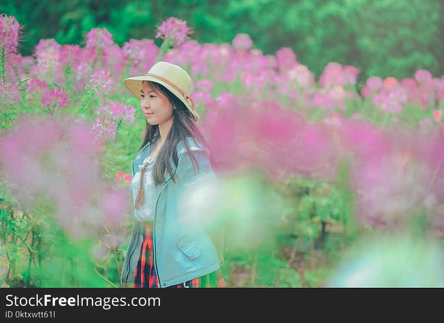 Woman Wearing Sun Hat and Blue Jacket Standing Surrounded by Flowers