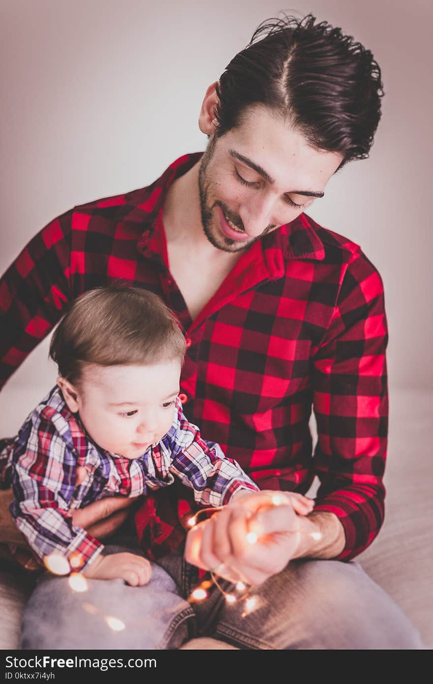 Man Wearing Red and Black Gingham Sports Shirt With Baby Beside Him