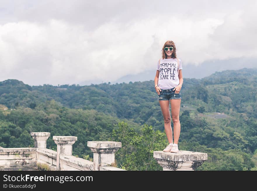 Woman Wearing White Shirt and Blue Denim Shorts Standing on Gray Concrete Stand