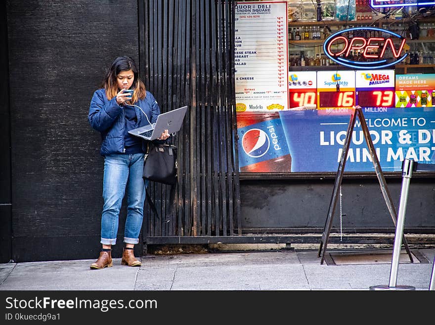 Woman in Blue Jeans Holding Macbook Pro Standing Against Black Wall