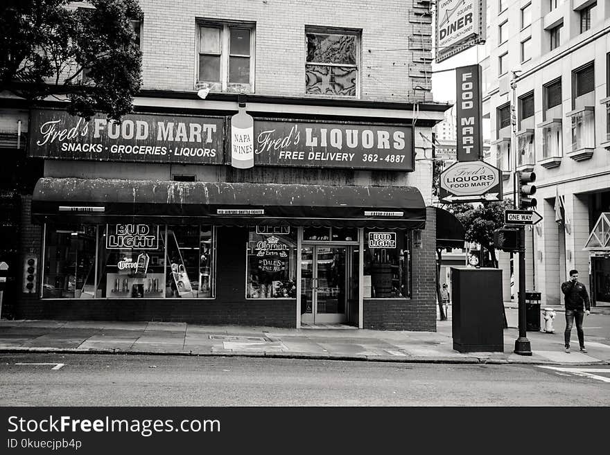 Greyscale Photo of Man Standing on Road Near Fred&#x27;s Liqours Building