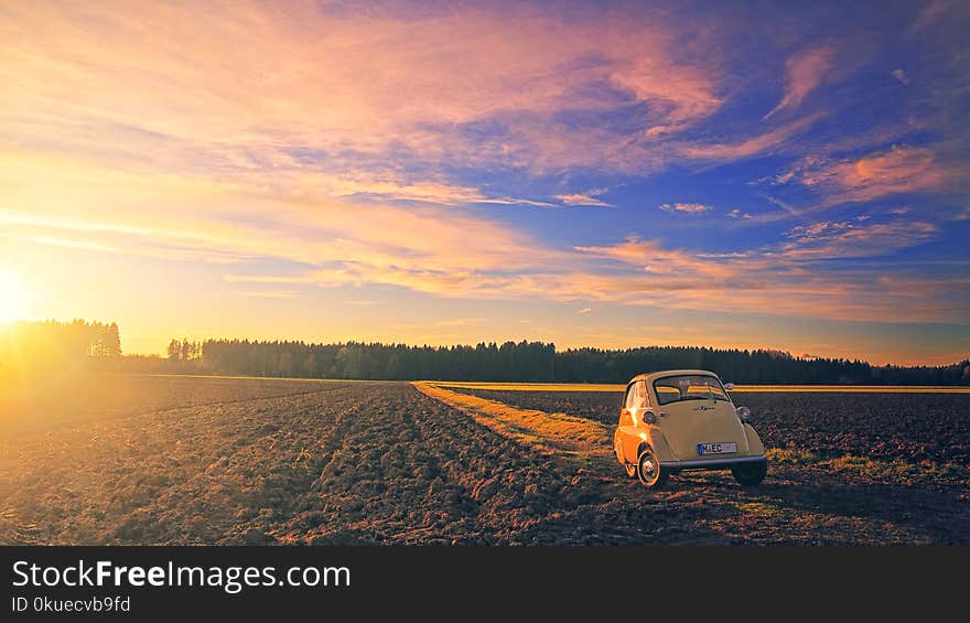 Yellow Classic Car Parked on Field Under Cloudy Sky at Golden Hour