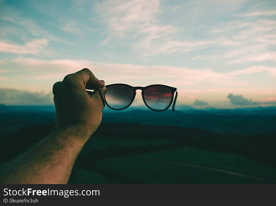 Person Holding Black Framed Sunglasses Under Blue Sky and White Clouds