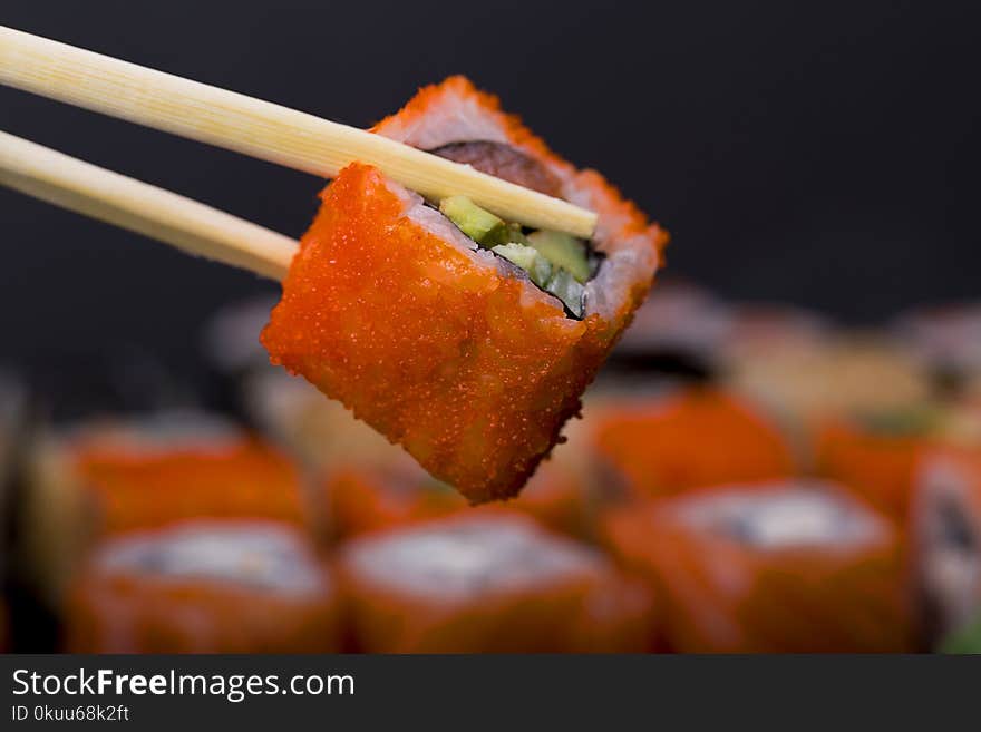 Fingers holding wooden sticks Сalifornia roll with salmon on black background