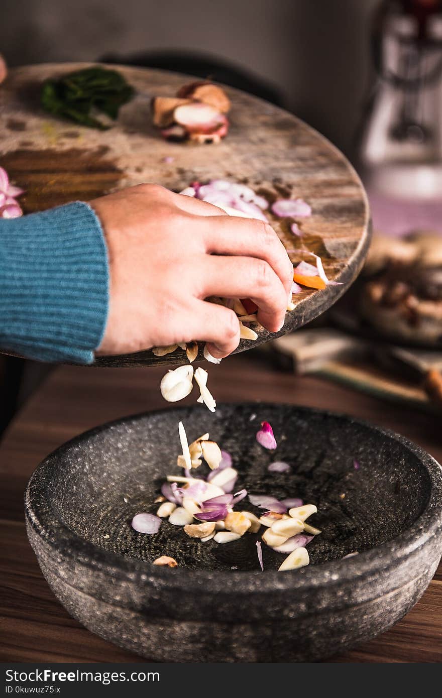 Person Pouring Sliced Spices from a Chopping Board to Black Bowl