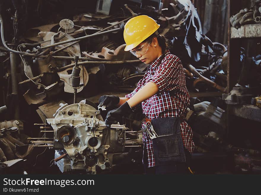 Woman Wears Yellow Hard Hat Holding Vehicle Part