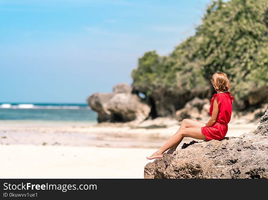 Woman in Red Dress Sitting on Brown Rock