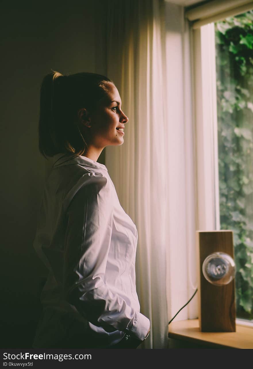 Woman Wearing White Long-sleeved Shirt Standing in Front of the Window With White Curtain