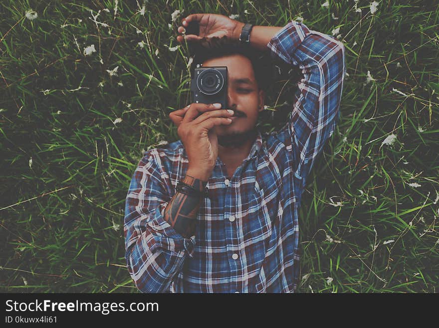 Man in Blue Dress Shirt Holding Camera White Laying on Grass