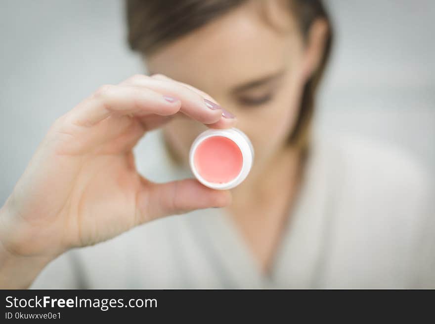 Person Holding Round White and Pink lipbalm