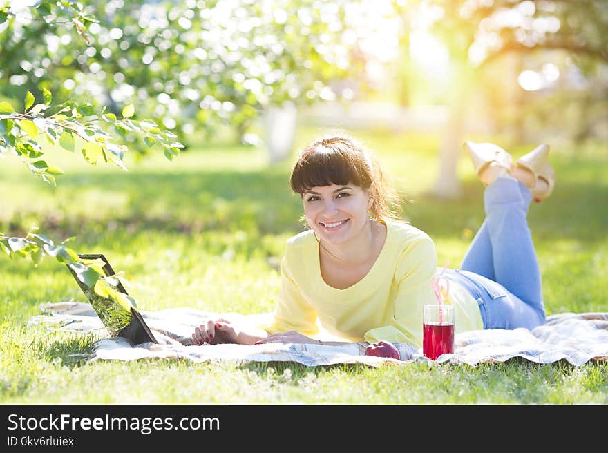 The brunette lies on the grass in the park and works with a laptop. Nearby is her breakfast - juice, fruit, biscuits. The brunette lies on the grass in the park and works with a laptop. Nearby is her breakfast - juice, fruit, biscuits.