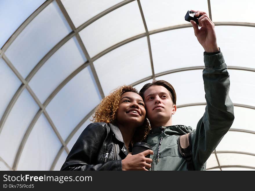 A modern beautiful African American girl smiles when together with a white guy they make selfi on an action camera. Cute