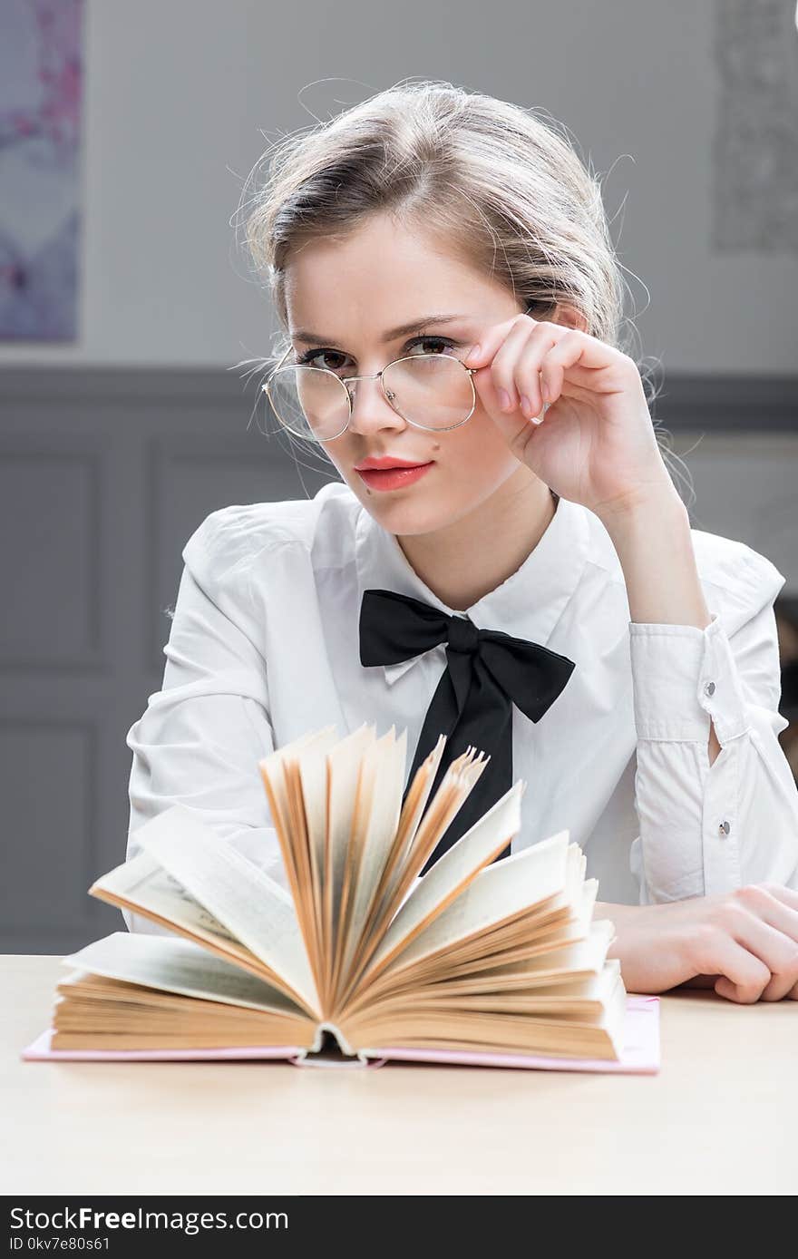 Charming successful businesswoman in glasses with a book at the table sits