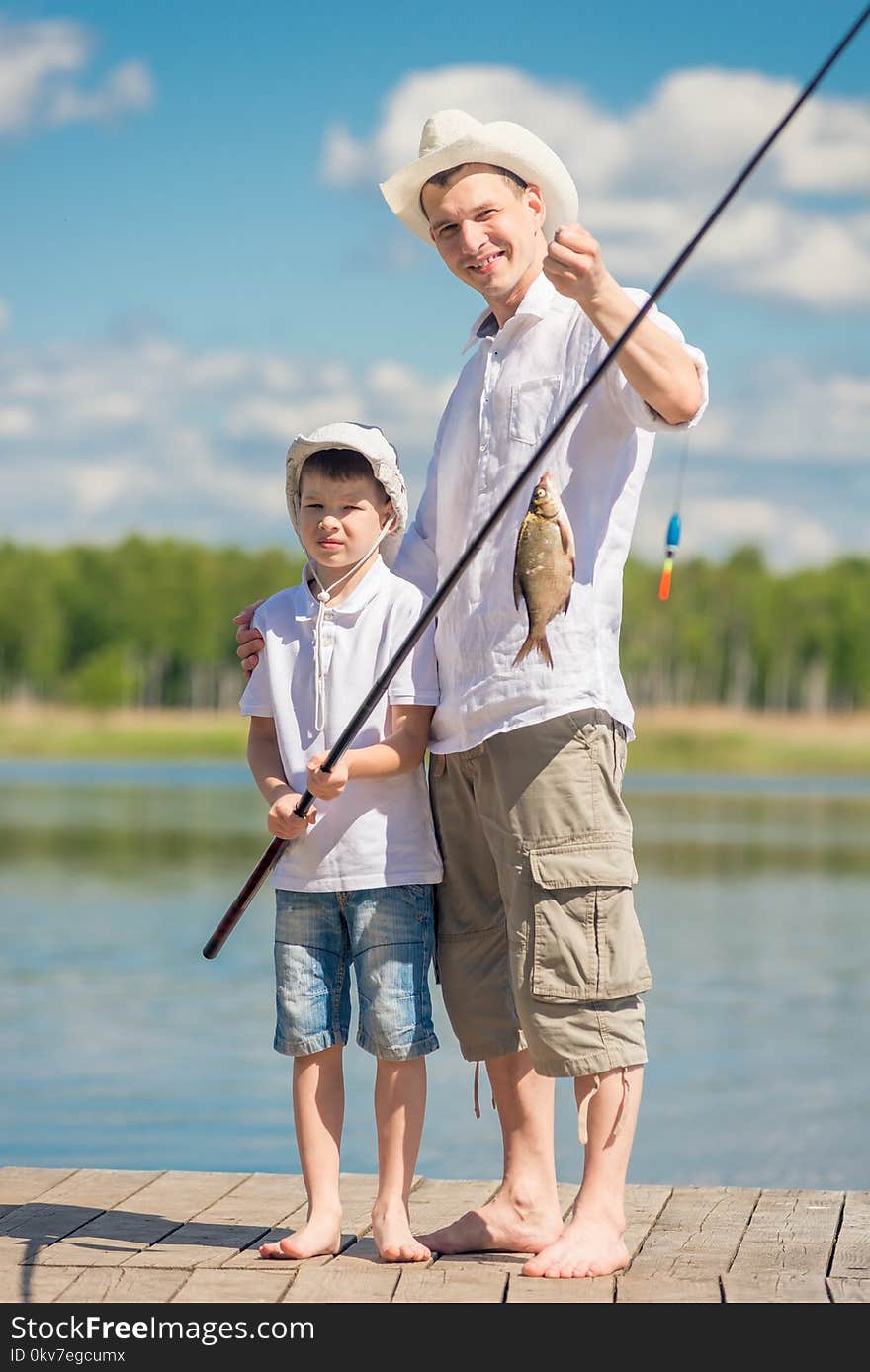 Vertical portrait of the father and son on the pier with a big fish on the hook, fishing on the lake