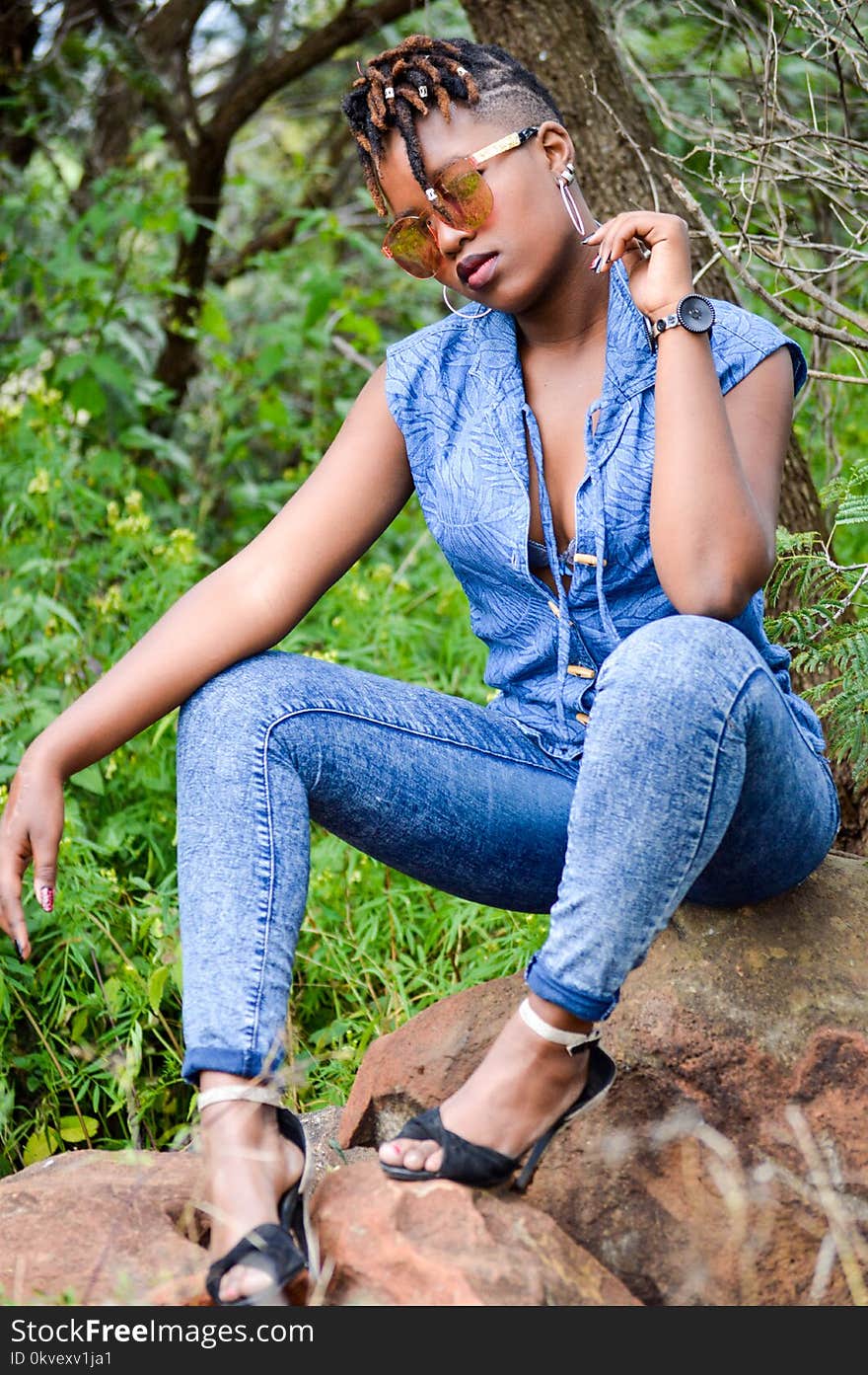 Woman Wearing Denim Pants Sitting on Brown Stone Near Plants