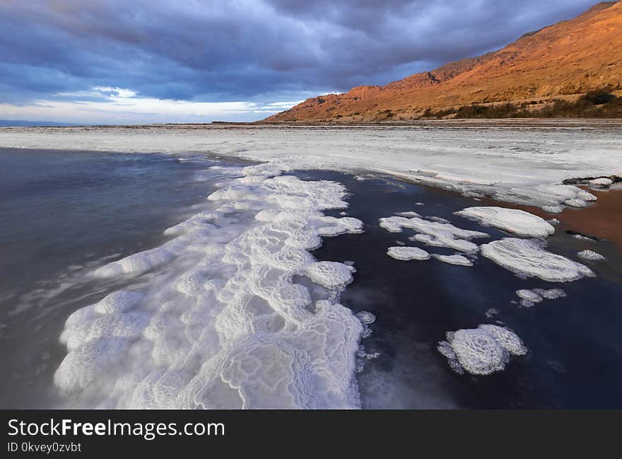 Body of Water With Bubbles Near Mountain