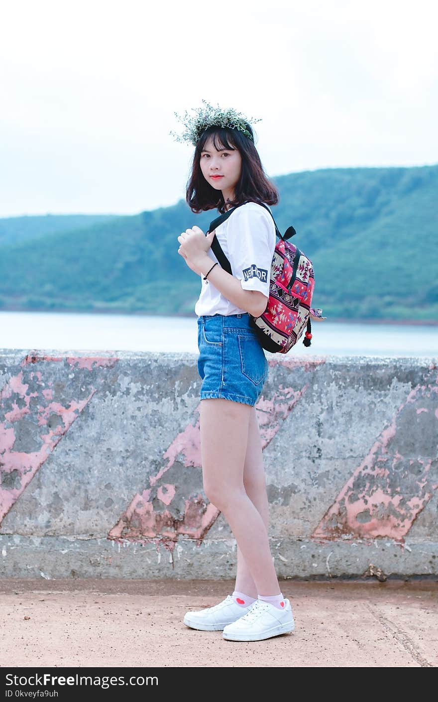 Photo Of Woman With Red And Black Backpack Standing Near Concrete Fence