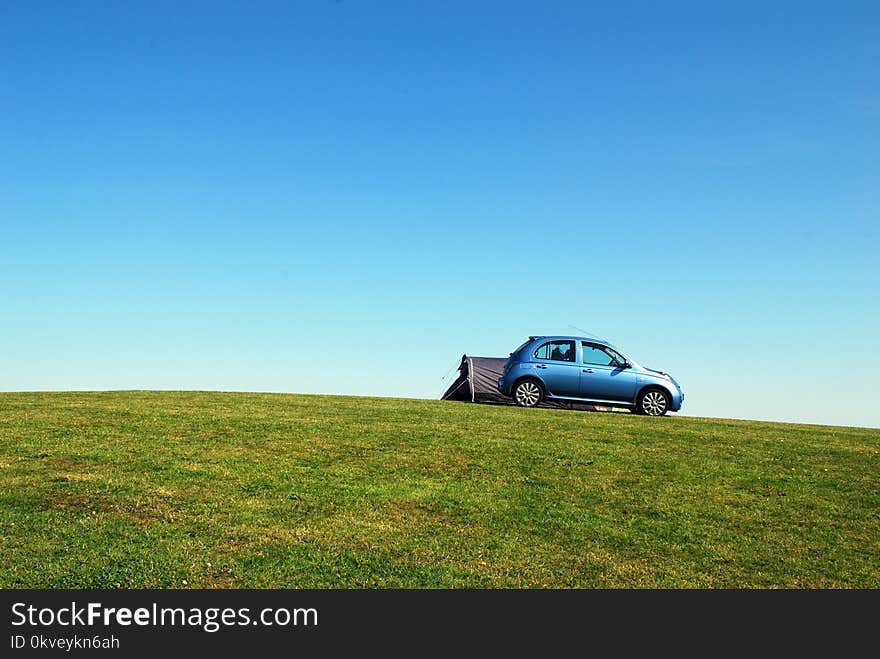 Blue Hatchback On Green Grass Field Under Blue Sky