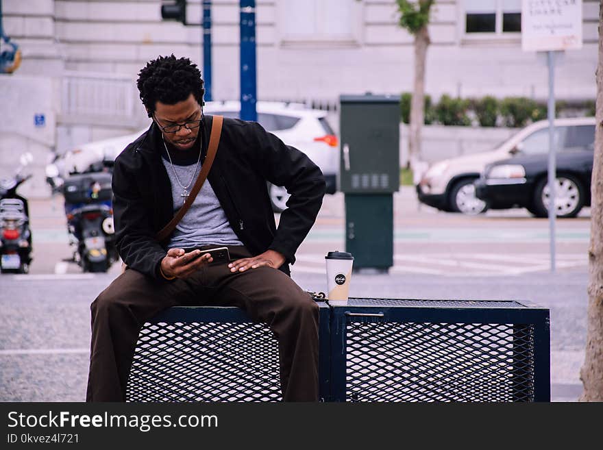 Man Wearing Black Bomber Jacket And Holding Smartphone