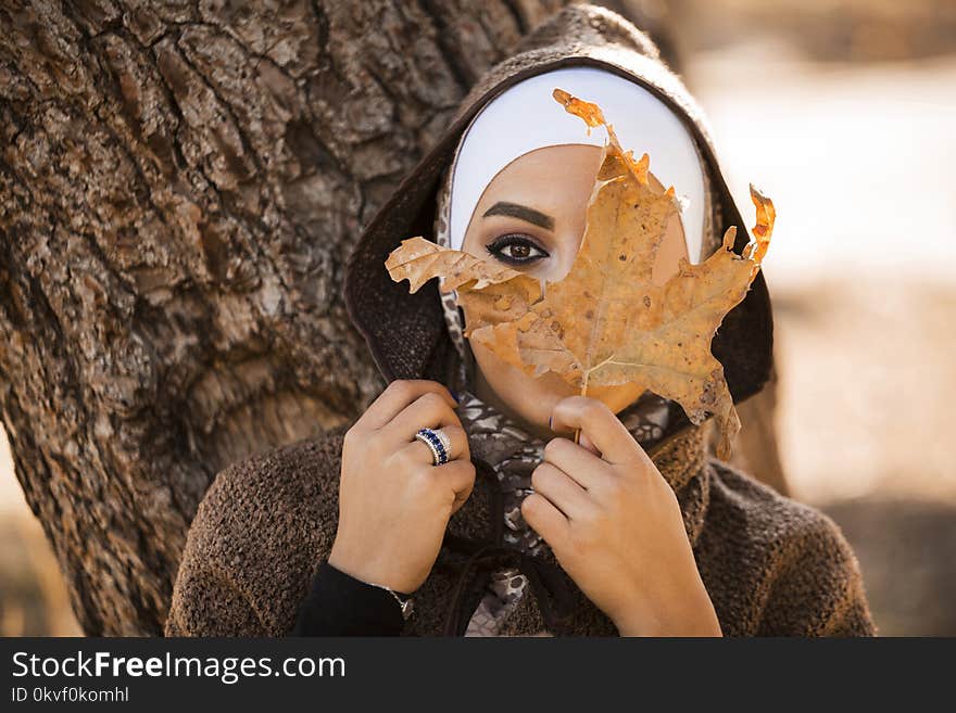 Woman Leaning on Brown Tree Holding Brown Leaf Covering Her Face