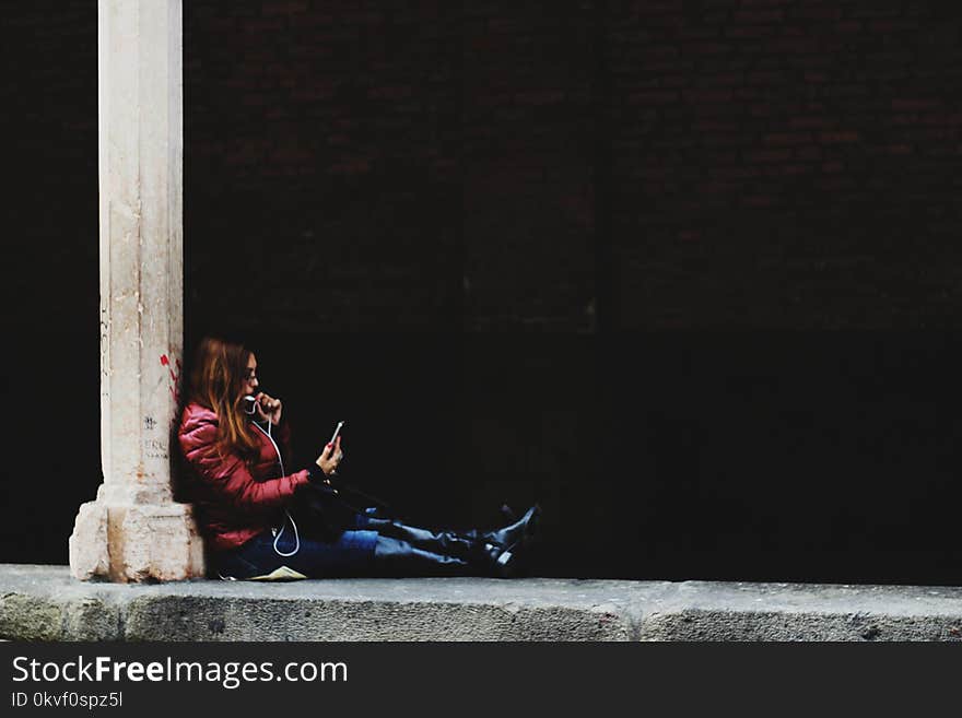 Photo of Woman Sitting on Pillar Holding Smartphone