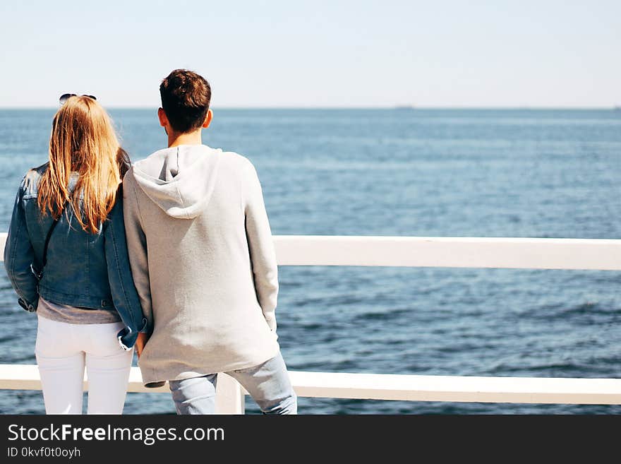 Man and Woman Beside Wooden Hand Rail Beside Body of Water