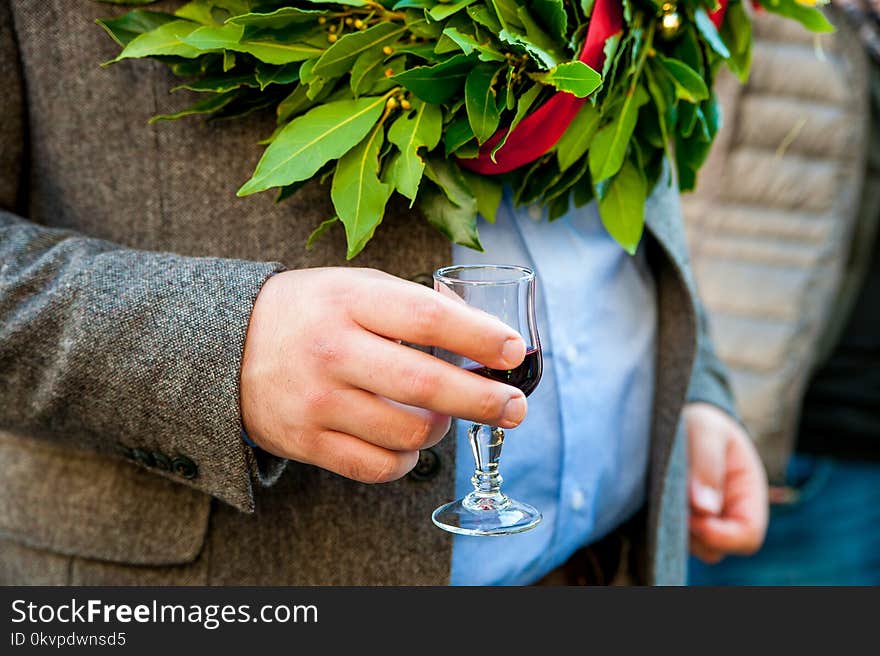 Young man hand holding glass of wine at traditional graduation ceremony with laurel crown