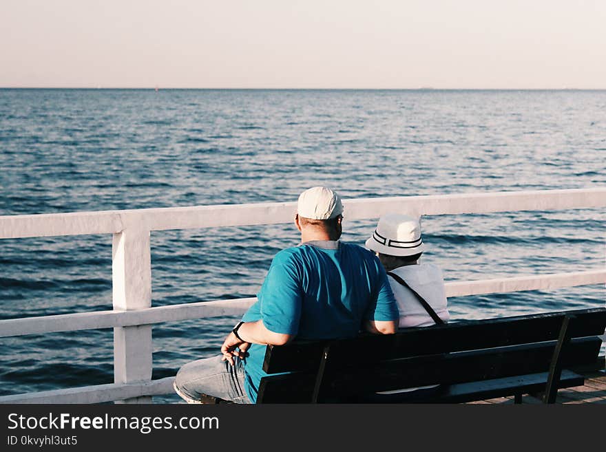 Man in Blue Shirt Beside Woman in White Shirt Sitting on Bench