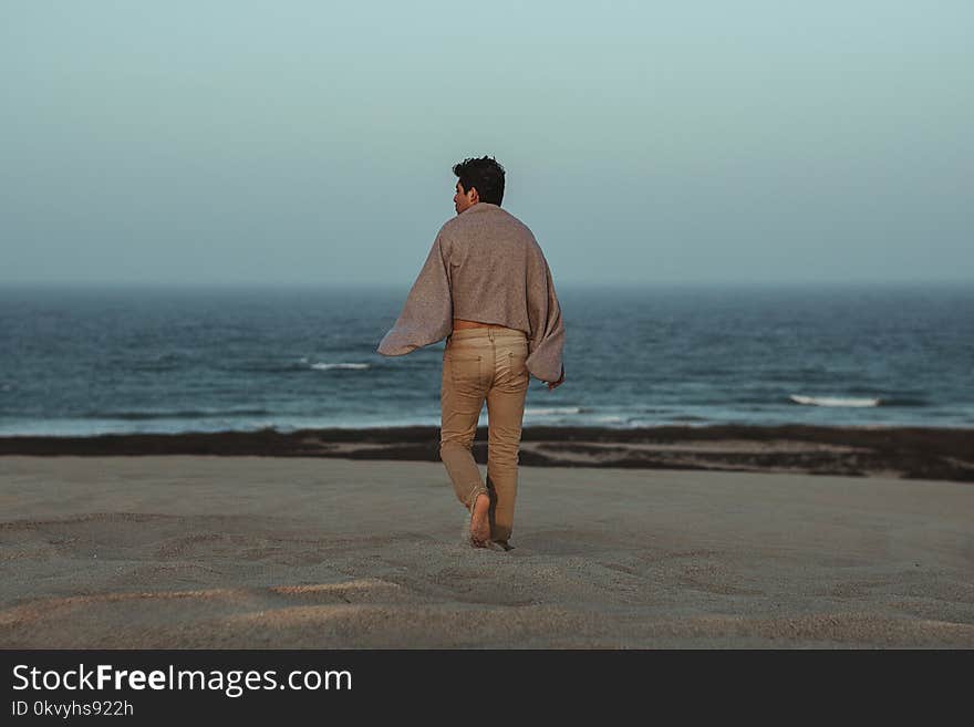 Man Walking Towards Shore With Grey Towel on Back