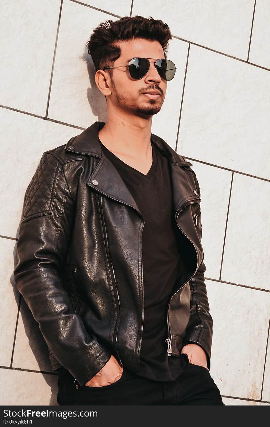 Man in Black Leather Jacket Leaning on White Concrete Wall