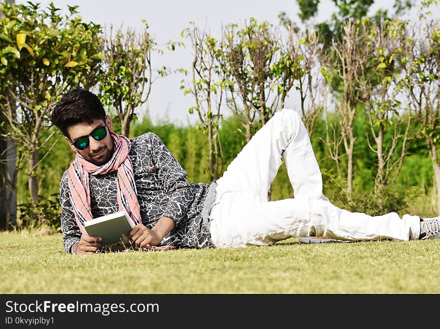 Man in White Pants Wearing Sunglasses Reading Book