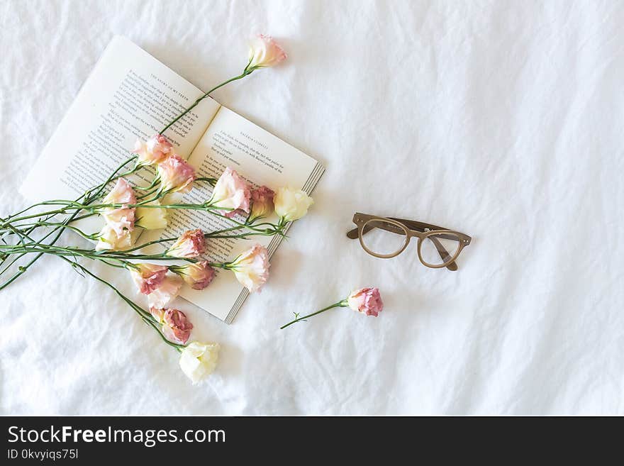 White and Pink Flowerson a book beside Eyeglasses