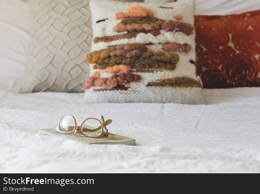 Brown Framed Eyeglasses on Book Near Pillows