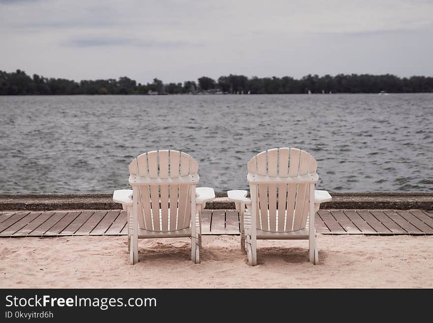 Two White Lounge Chairs Beside Body of Water