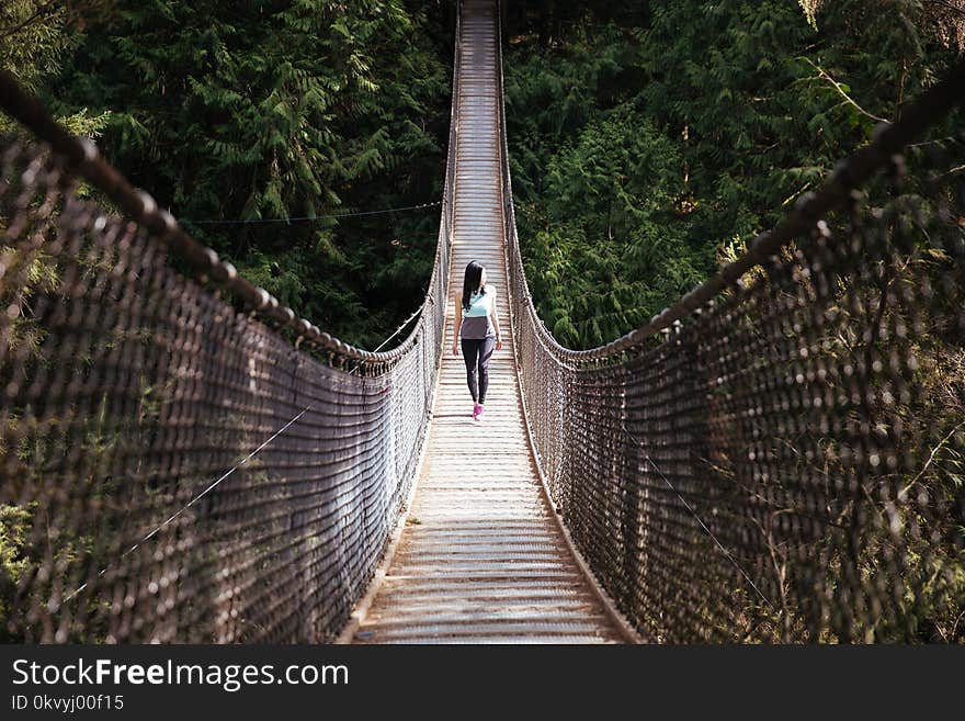 Woman Wearing Blue Sleeveless Shirt Walking on Bridge at Daytime