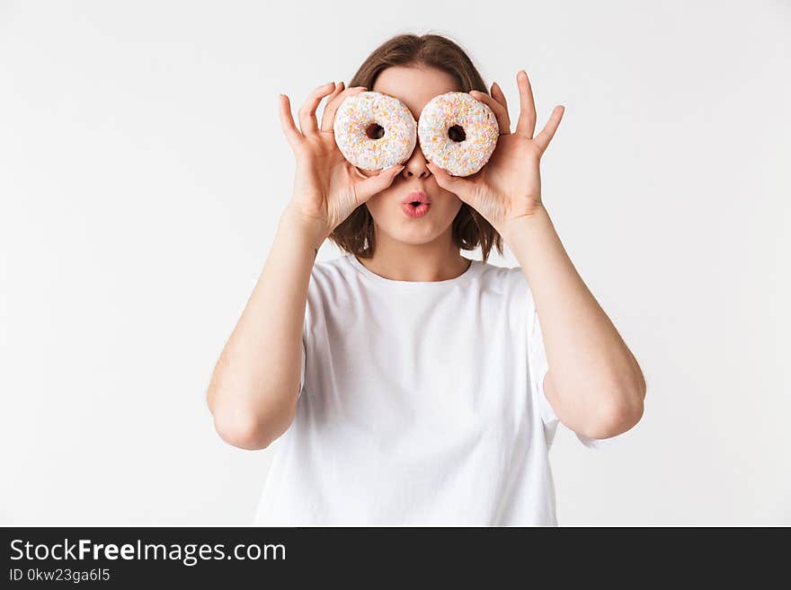 Portrait of a smiling young woman holding two donuts at her face isolated over white background