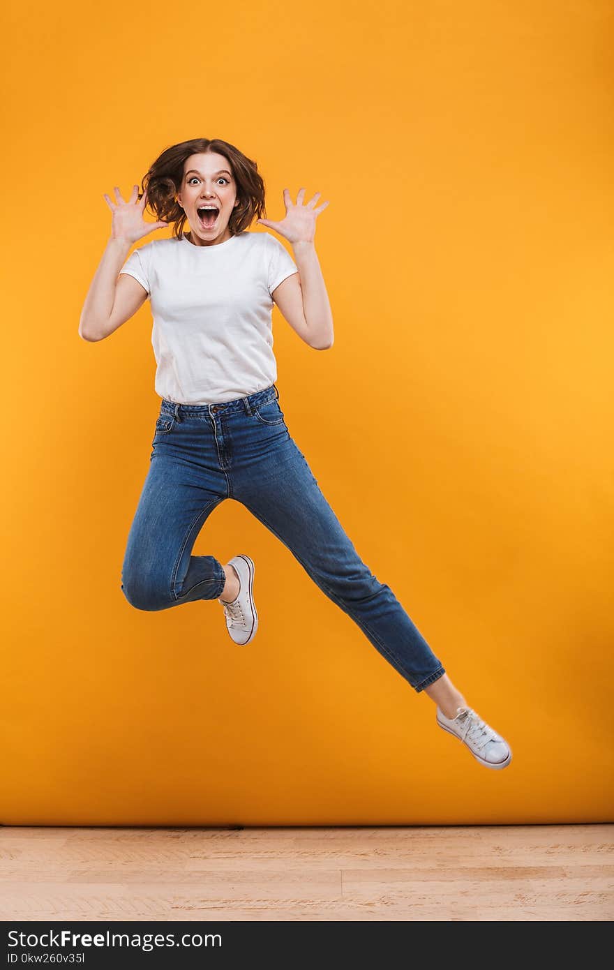 Photo of emotional young woman jumping isolated over yellow background. Looking camera.
