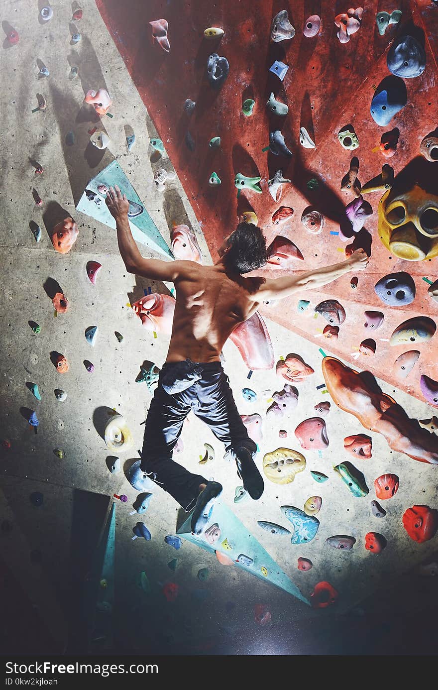 A man climber climbs indoors in bouldering gym. Athletic man climbing up on practice wall