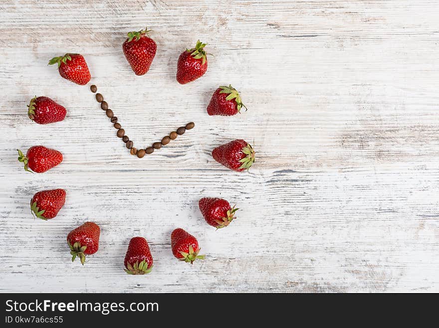 strawberry clock with arrows from coffee beans showing the time thirteen hours fifty-five minutes or one hour fifty-five minutes on a wooden old background in the kitchen. Flat Lay. Background for a postcard, banner, site, advertisement