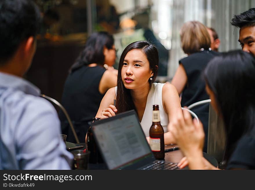 Woman Wearing White Top Sitting Near Table With People