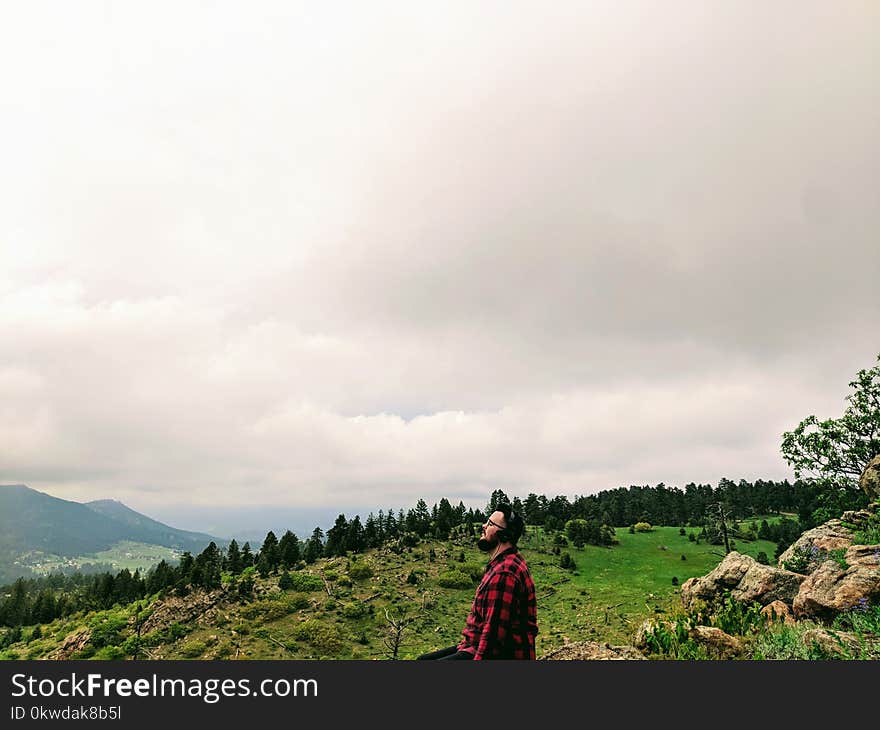 Man Wearing Red and Black Plaid Shirt Standing on Green Grass Hill