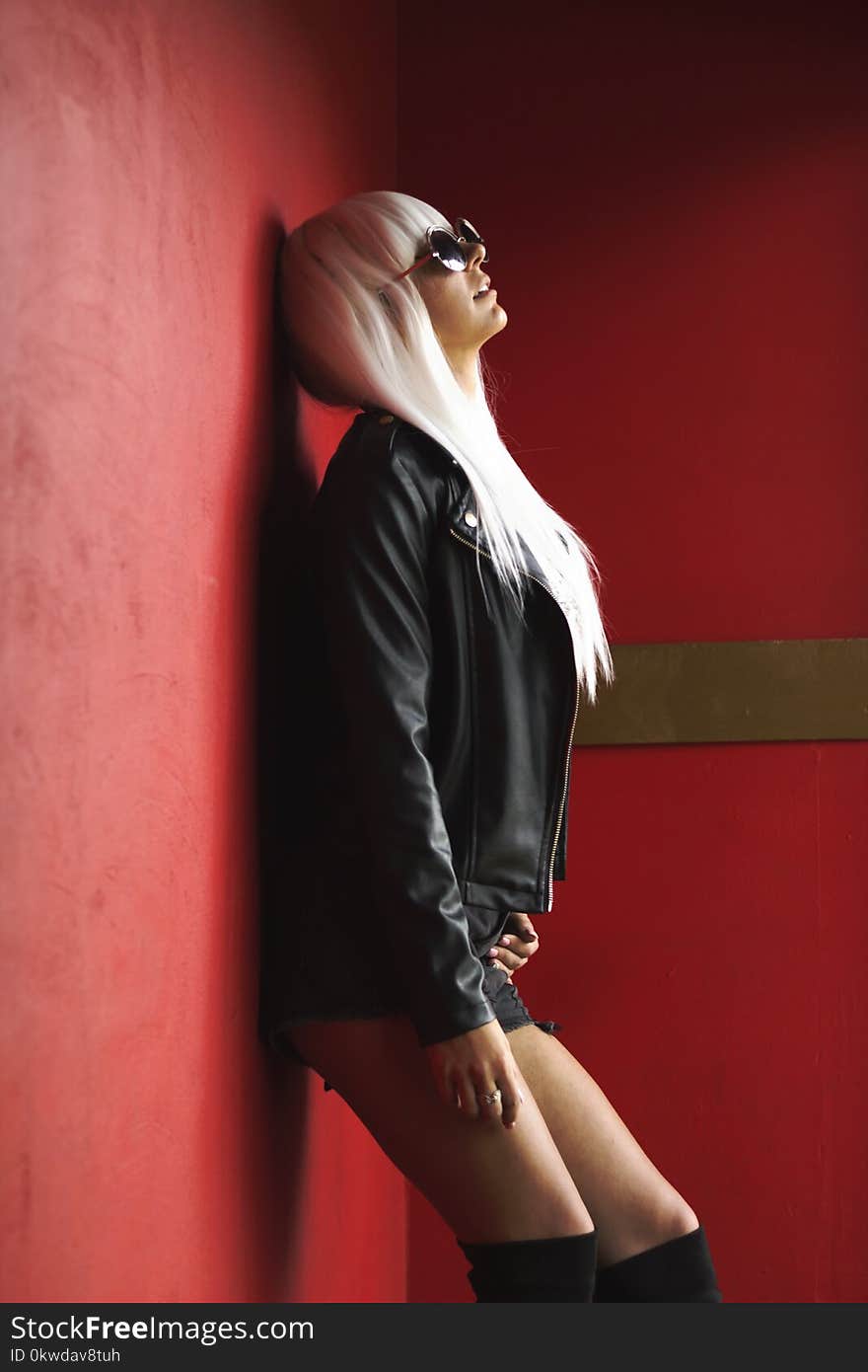 Woman Wearing Black Leather Jacket Leaning On Red Wall