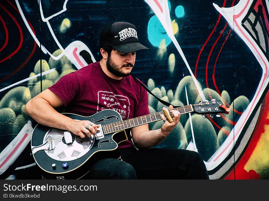 Man in Red Shirt Playing Resonator Guitar Near Wall With Black and Green Painting