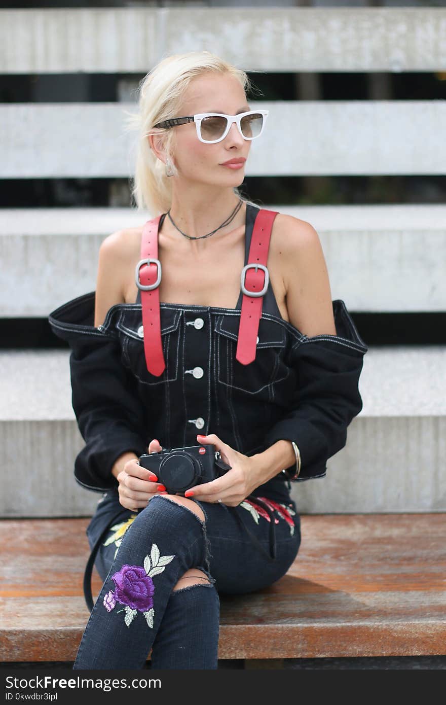 Woman in Black Denim Off-shoulder Top Sitting on Board While Holding Black Camera