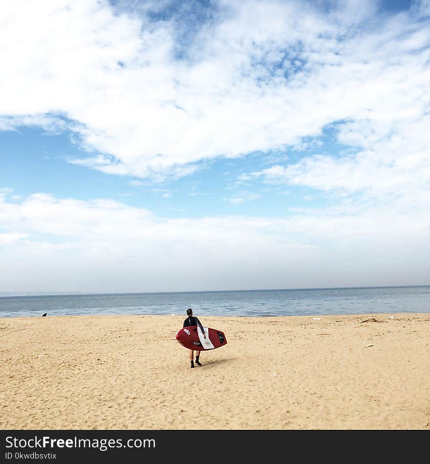 Person Holding Red And White Surfboard Near Sea Under Blue Sky