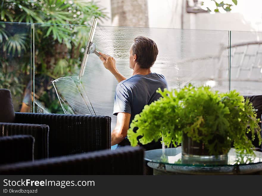 Man in Gray Shirt Cleaning Clear Glass Wall Near Sofa