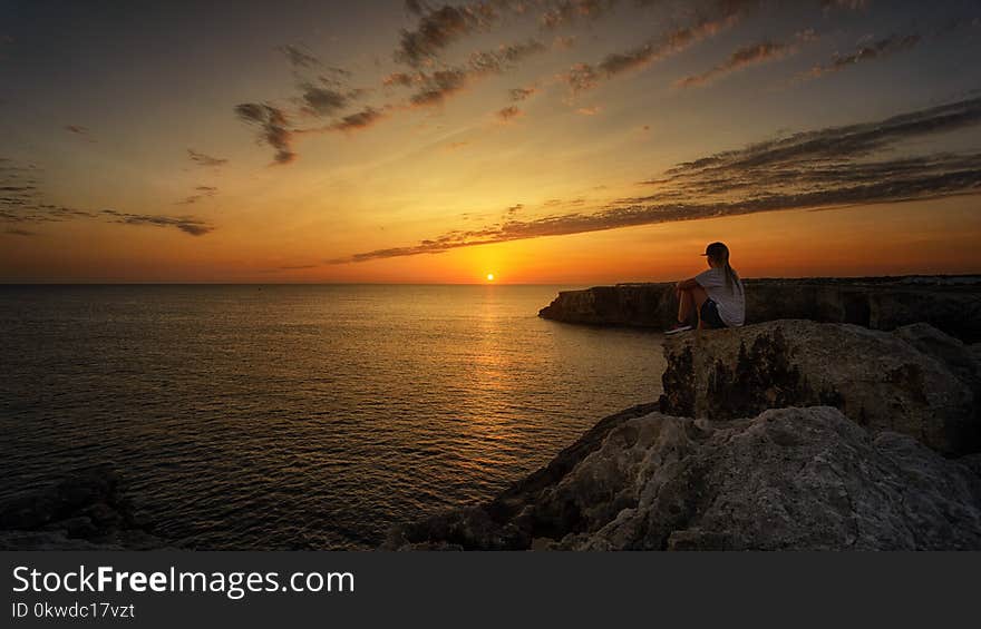 Photo of Person Sitting on Rock During Sunset