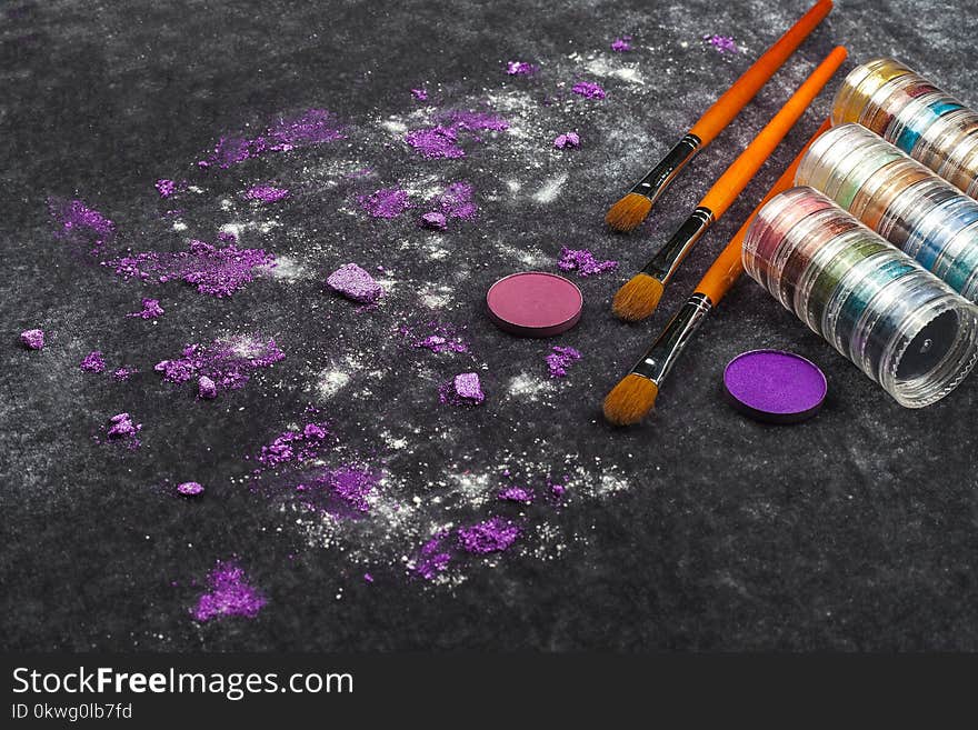 Collection of brushes with palette near pink and purple loose eye shadows lying on a black background. concept of professional cosmetics. free space for text. Collection of brushes with palette near pink and purple loose eye shadows lying on a black background. concept of professional cosmetics. free space for text