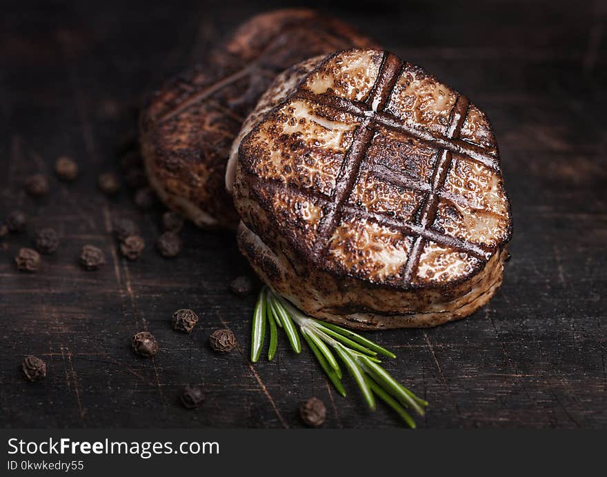 Grilled juicy beef pork steak slice on wooden background with pepper and rosemarine herb